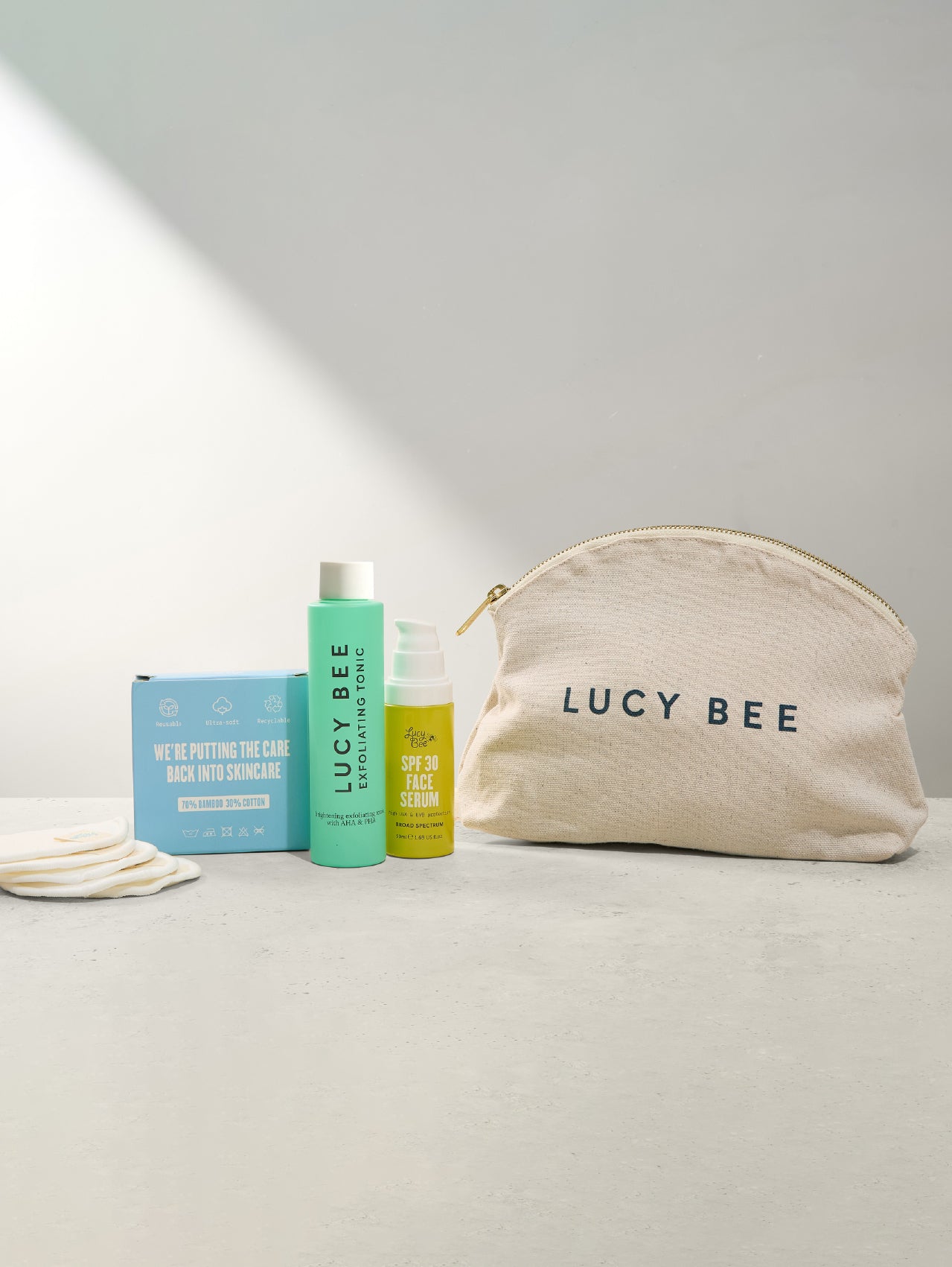 Lucy Bee skincare products including a pouch, box, and bottles on a light surface with a neutral background.