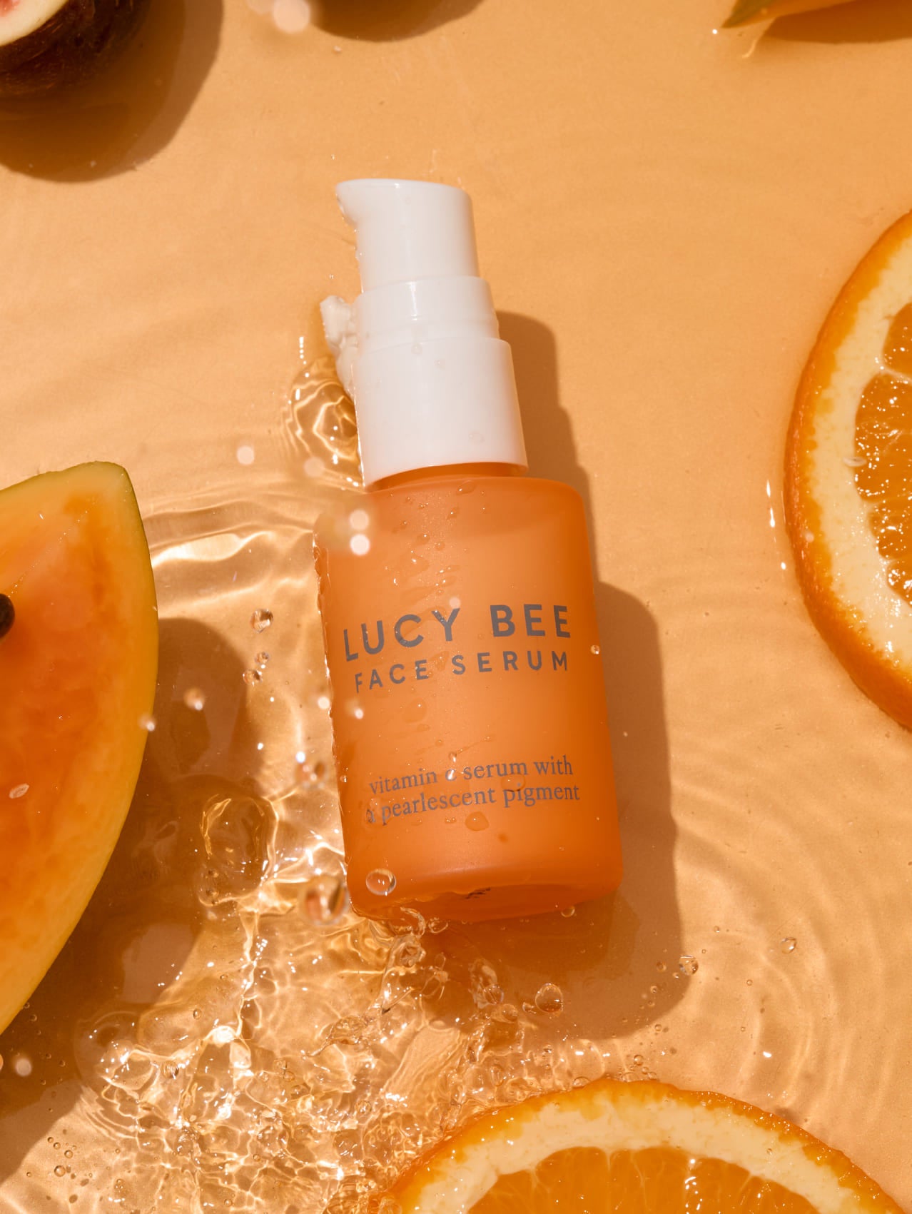 Lucy Bee face serum bottle on a peach-colored background with fruit slices