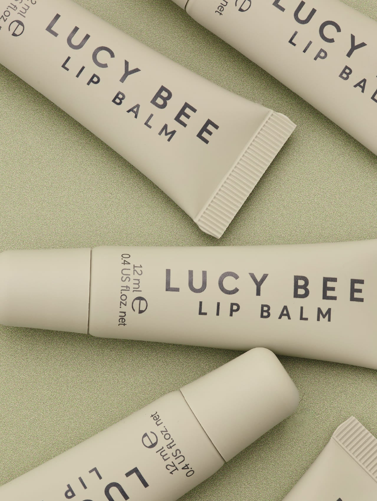 Multiple tubes of Lucy Bee lip balm on a light green background