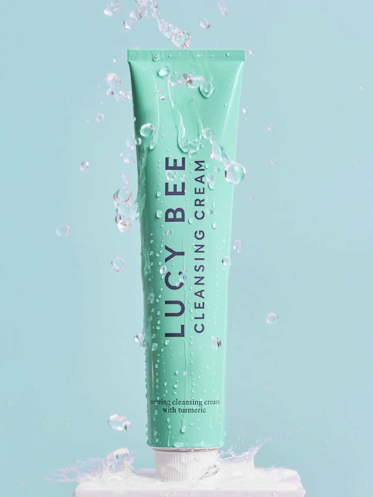 Tube of Lucy Bee cleansing cream with water droplets on a light blue background