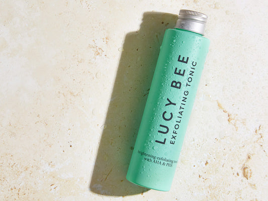 lucy bee exfoliating tonic on cream background with water droplets