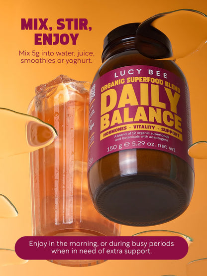 Lucy Bee Daily Balance superfood blend bottle with a drink in the background on an orange background. Lucy Bee organic daily balance to support stress and times when you may feel out of balance