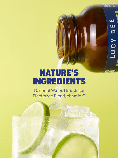 Lucy Bee supplement bottle being poured into a glass with lime slices on a yellow background. Lucy Bee electrolyte powder UK with coconut water