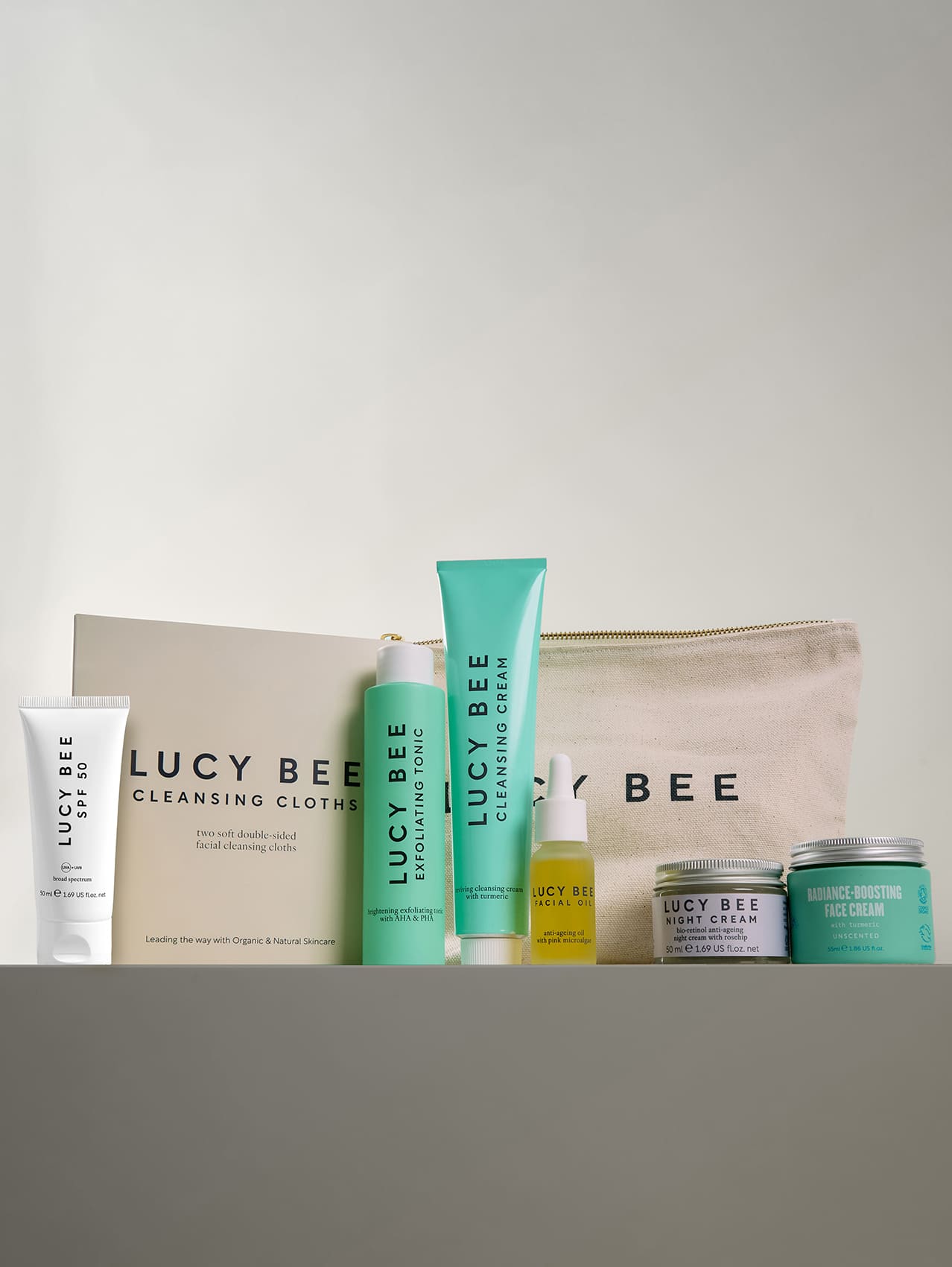 Lucy Bee skincare products including cream, lotion, and cleanser on a gray surface with a white background.