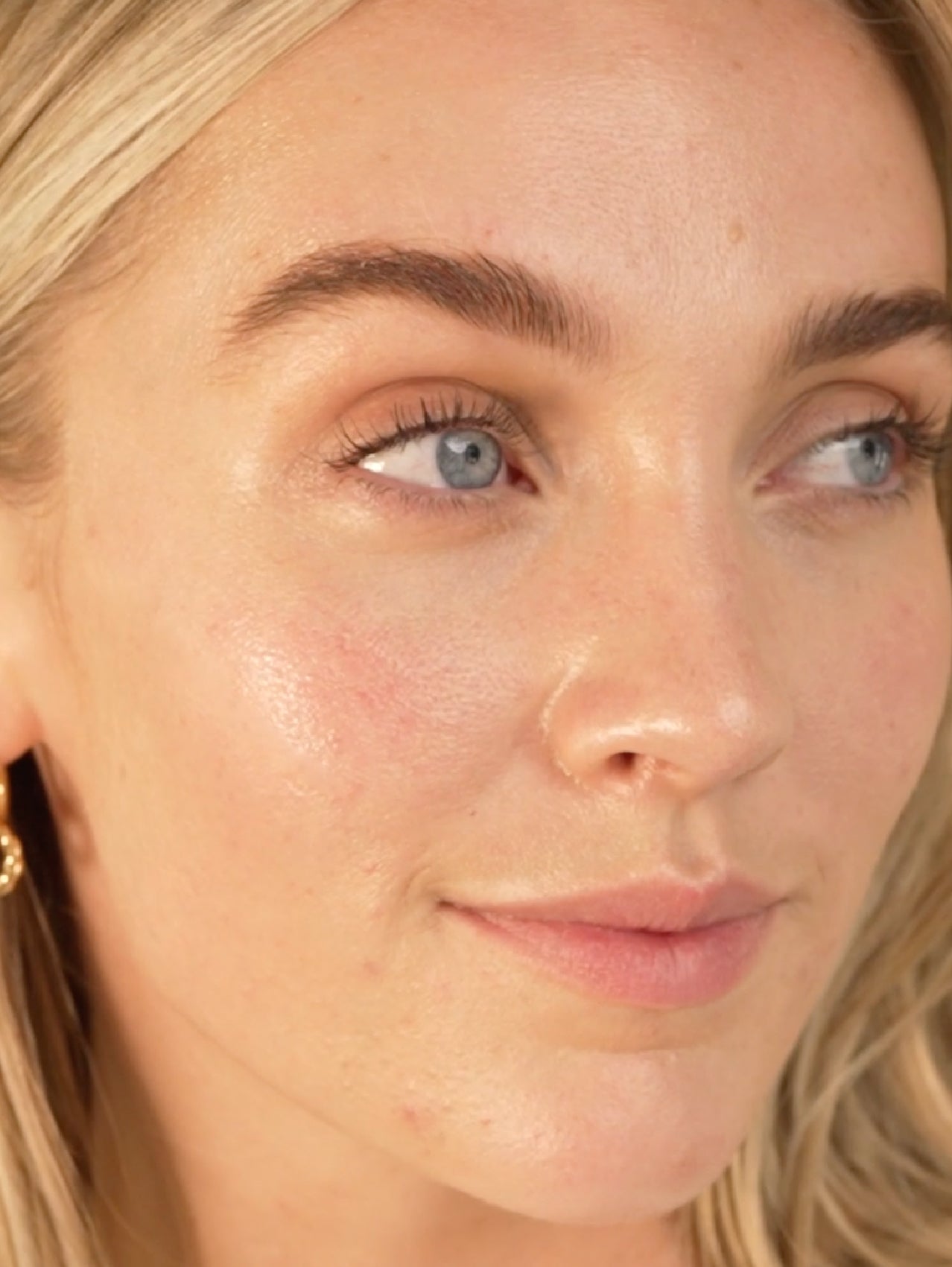 Close-up of a person with blonde hair and blue eyes, wearing gold earrings.
