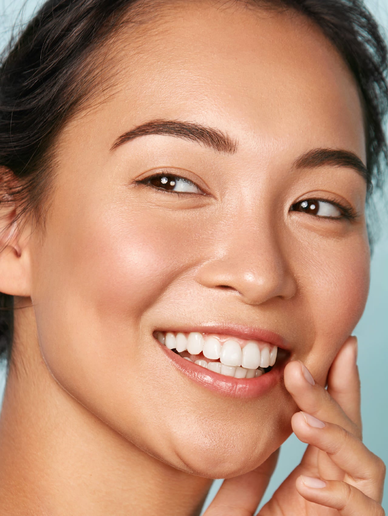 Close-up of a woman's face with a clear complexion against a light blue background