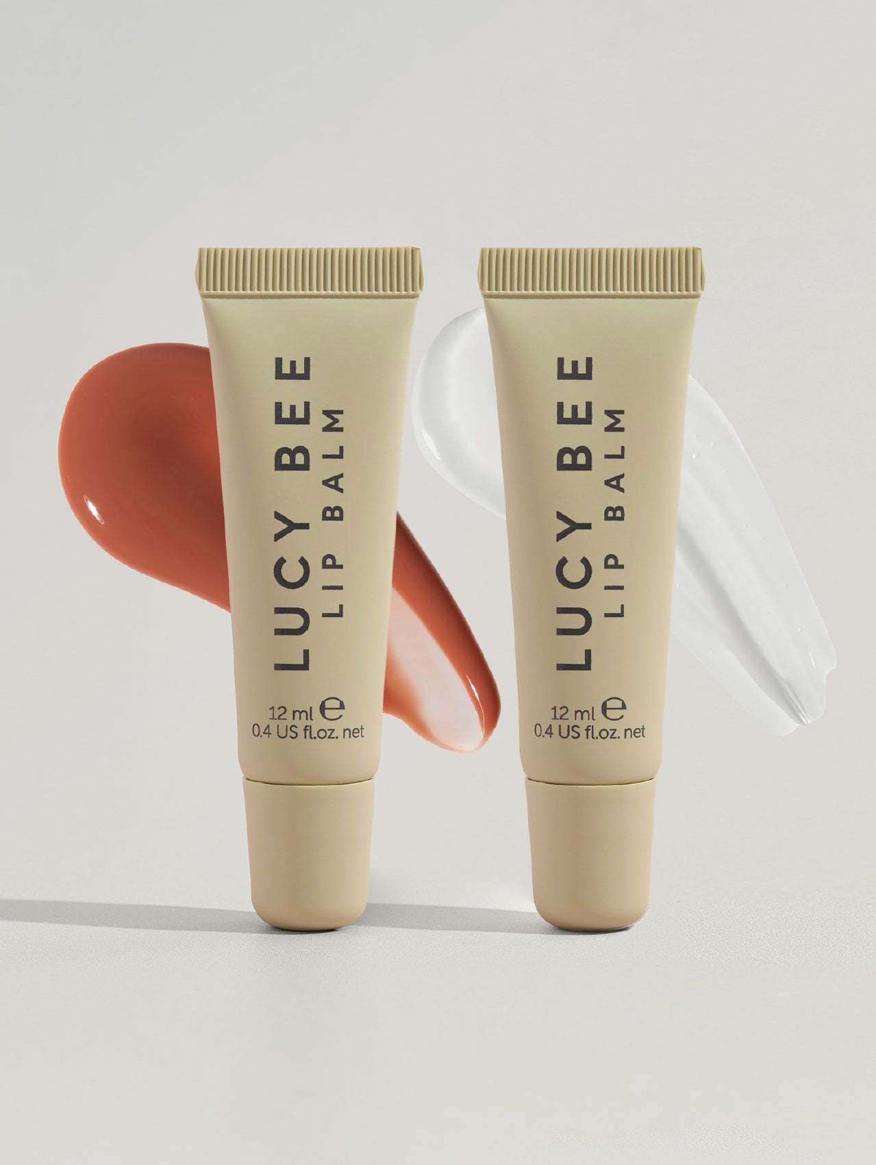 Two tubes of Lucy Bee lip balm on a light gray background