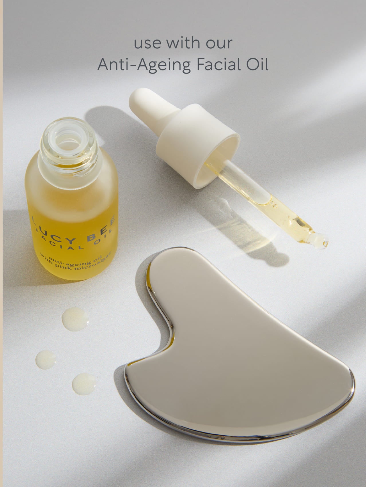 Anti-ageing facial oil with dropper and gua sha tool on a light background