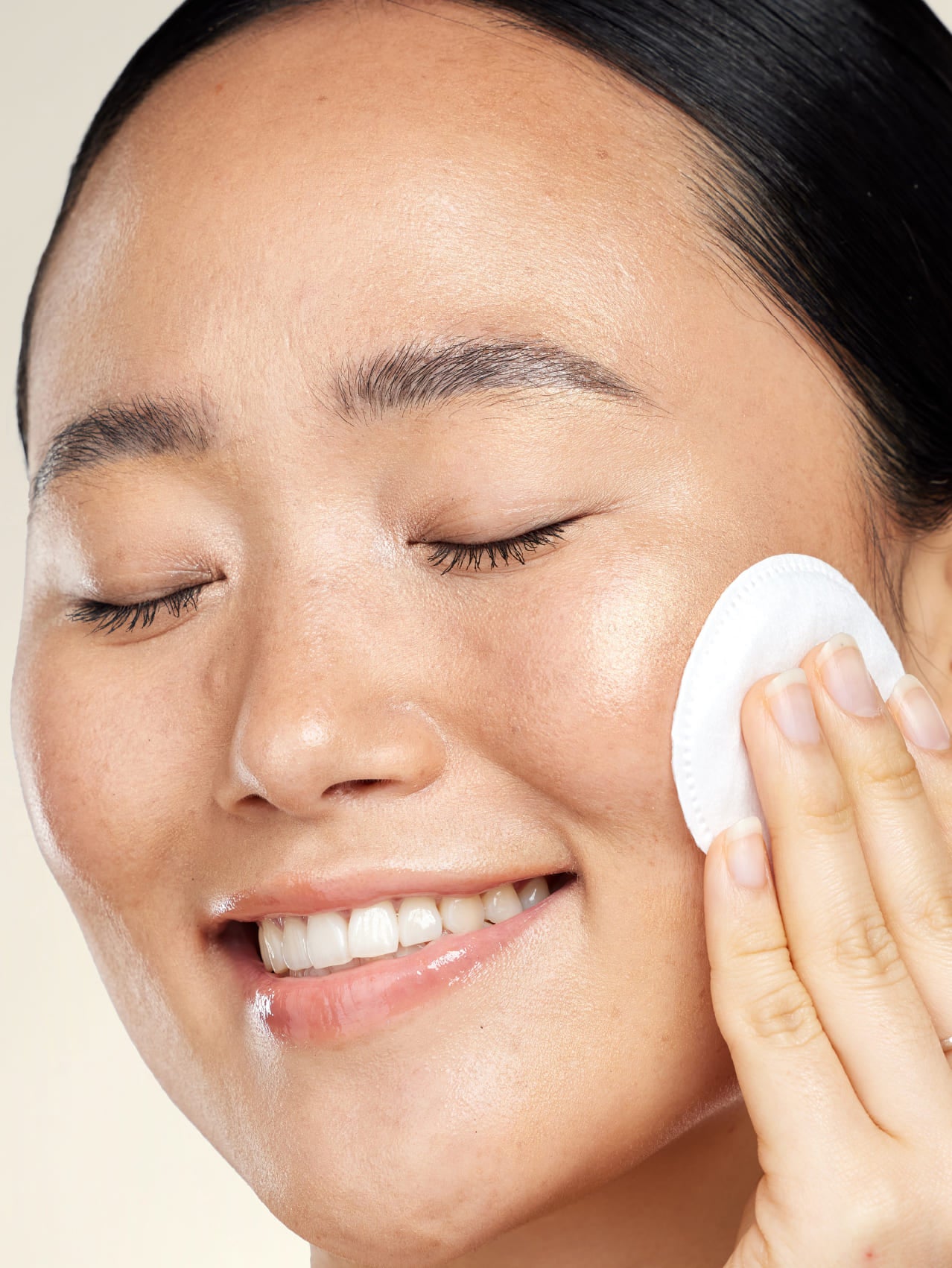 Person using a white cotton pad on their face against a beige background