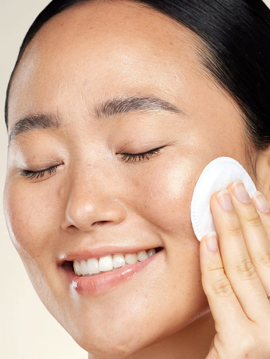 Person using a white cotton pad on their face against a beige background