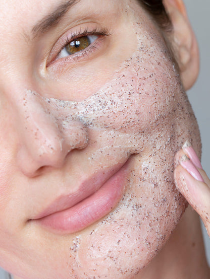 Close-up of a person applying Lucy Bee facial scrub to their skin.