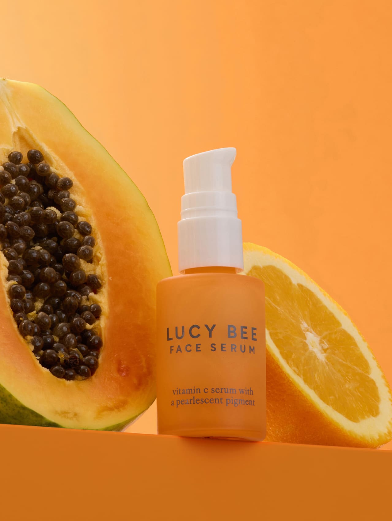 Lucy Bee face serum bottle with a papaya and orange on an orange background