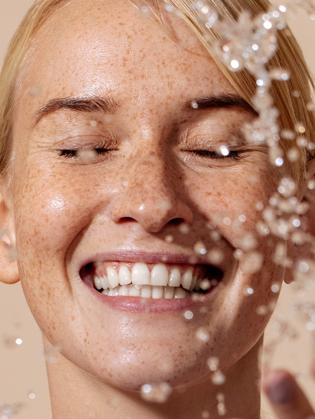 Woman with freckles smiling under a shower of water droplets.