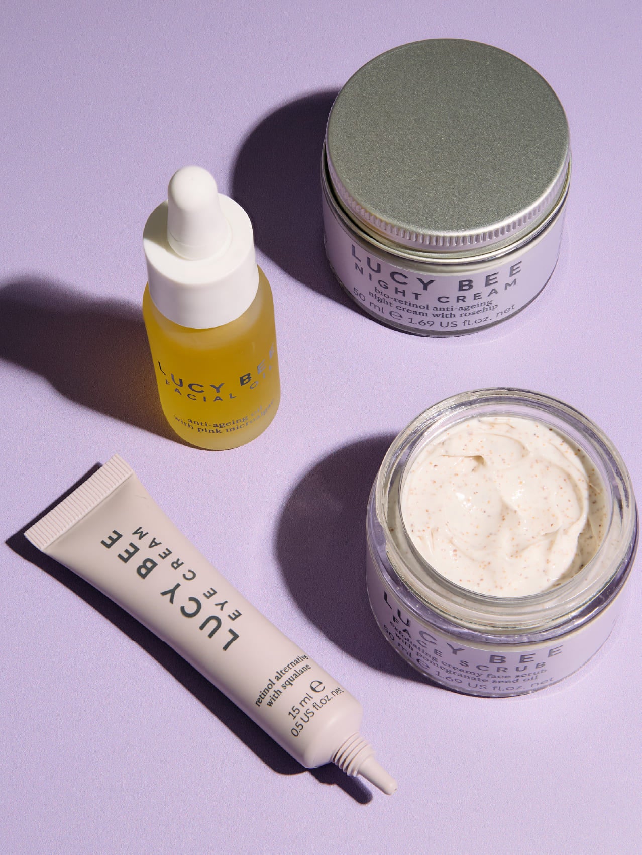 Set of Lucy Bee skincare products including a serum, cream, and scrub on a light purple background.