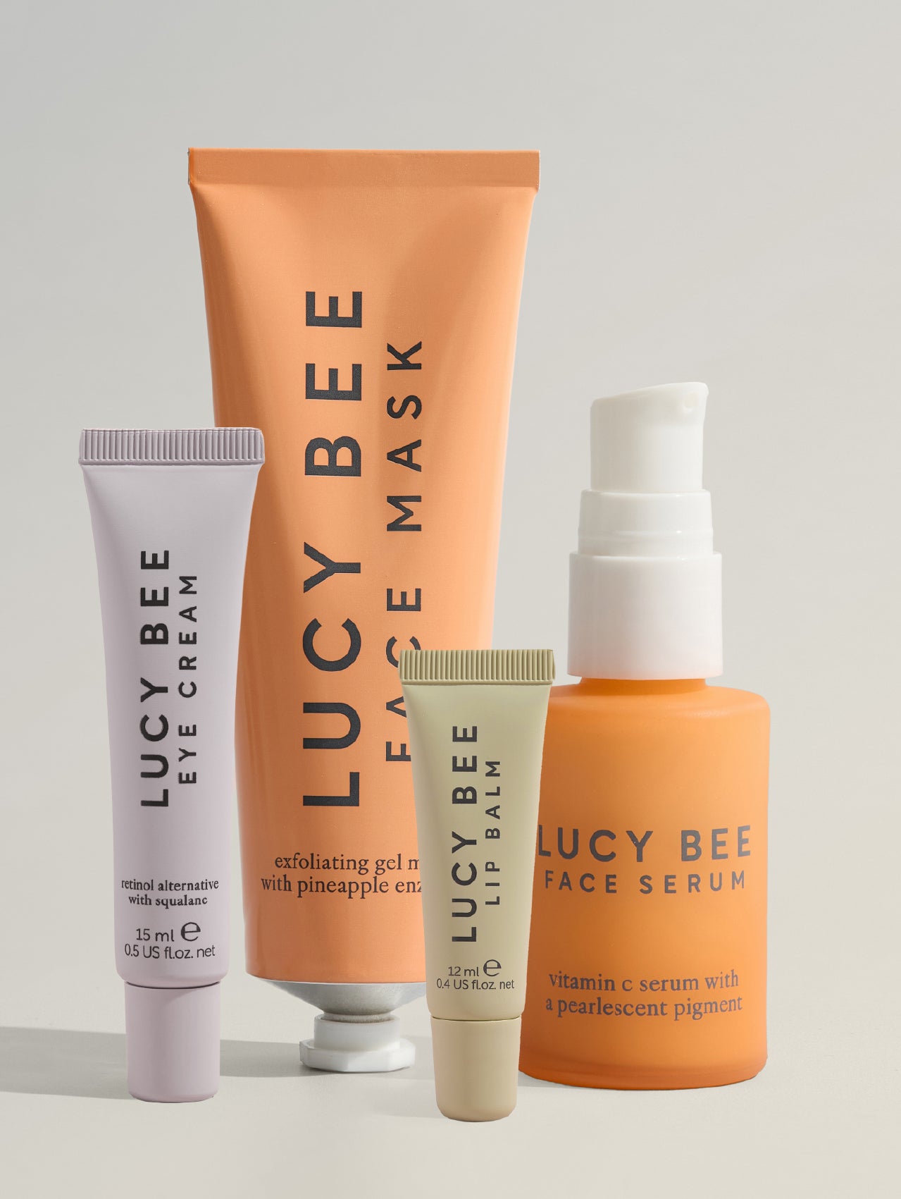 Set of Lucy Bee skincare products including eye cream, face mask, lip balm, and face serum on a light gray background.
