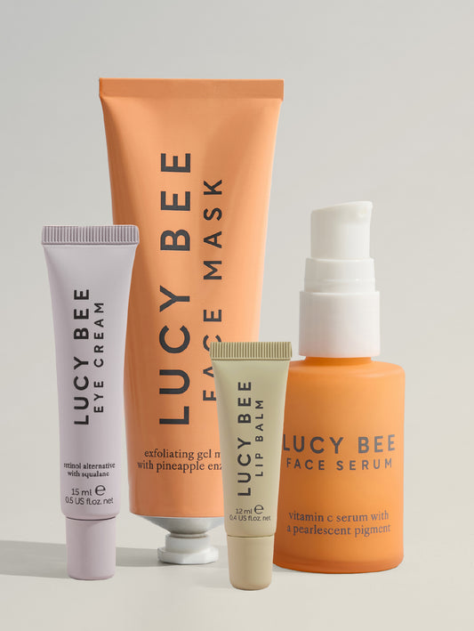 Set of Lucy Bee skincare products including eye cream, face mask, lip balm, and face serum on a light gray background.