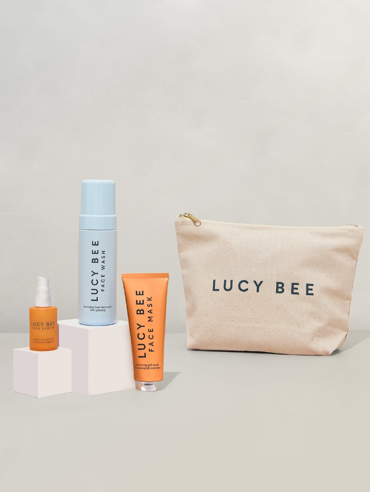 Lucy Bee skincare products including a pouch, bottle, and mask on a light gray background
