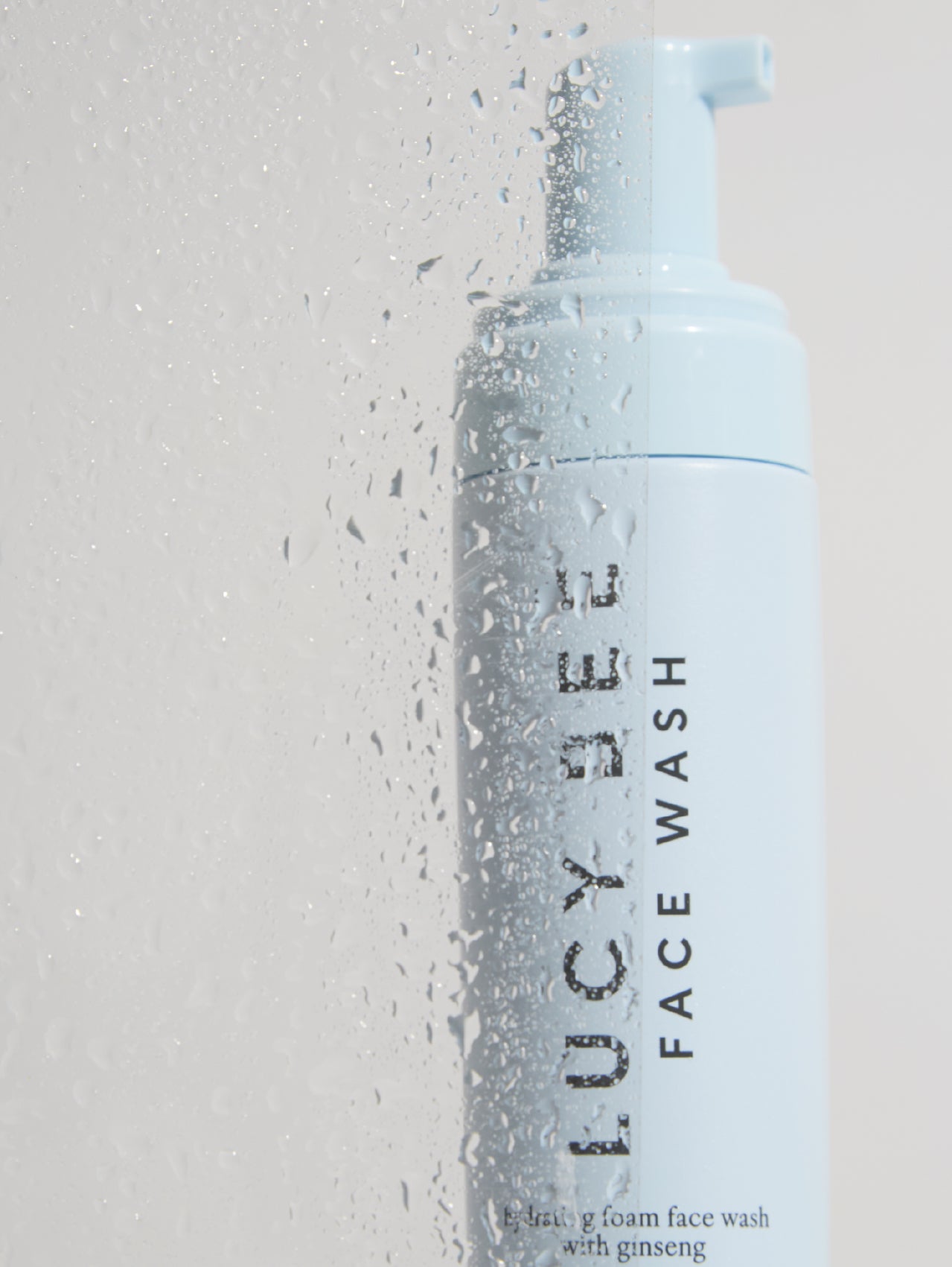 Lucy Bee face wash bottle with water droplets on a light gray background