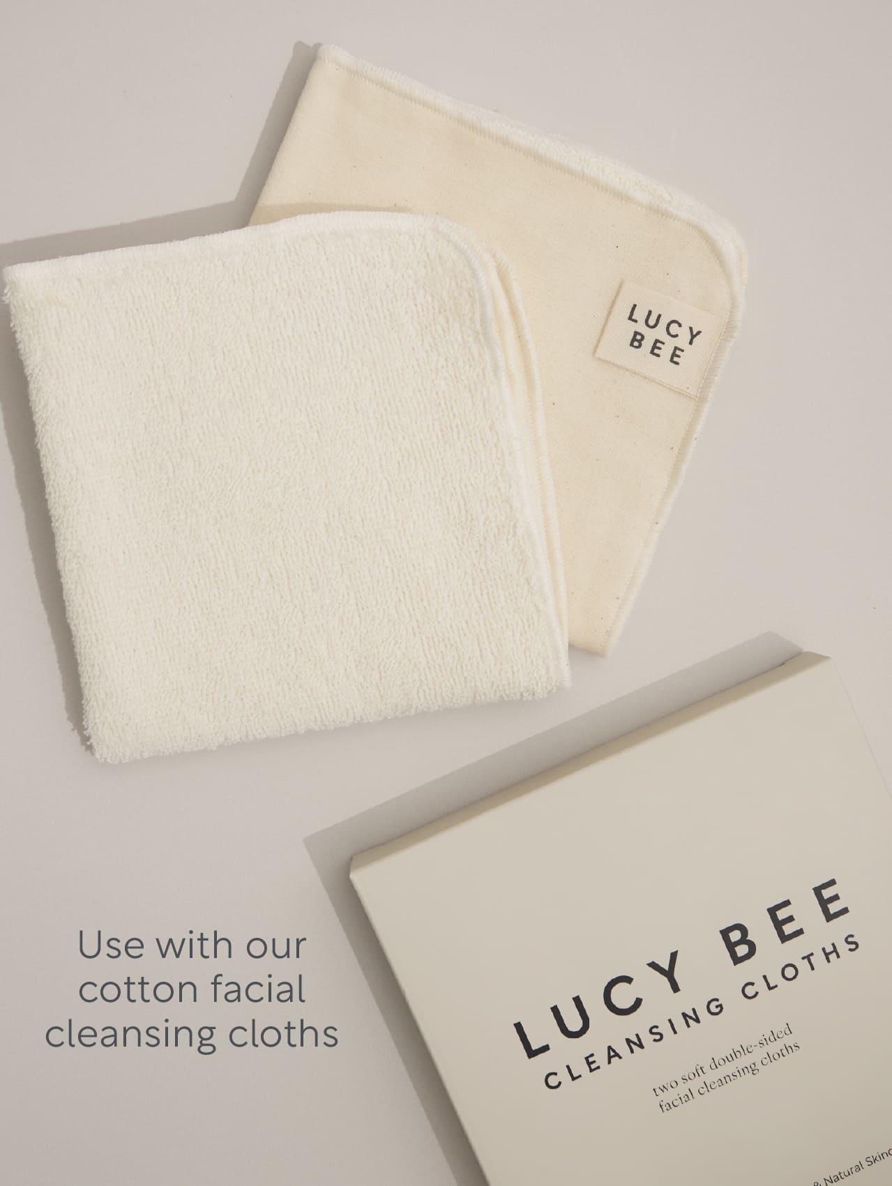Two white cotton facial cleansing cloths with a Lucy Bee box on a light gray background.